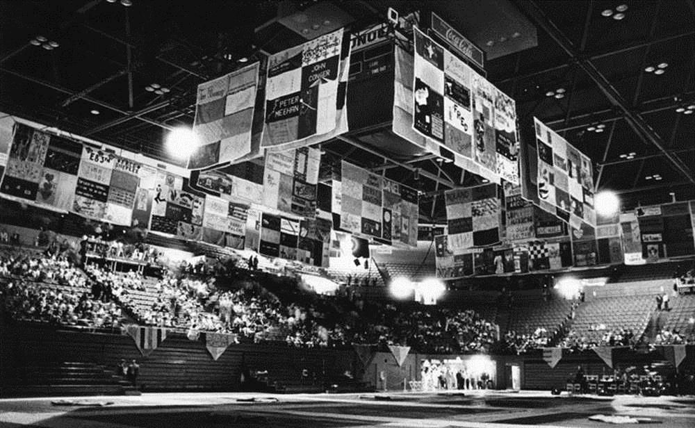 Panels of the seven-ton patchwork quilt, which memorializes those who have died of AIDS, hang from the ceiling and have been placed on the floor inside Pauley Pavilion on the UCLA campus in preparation for a fund-raising event. At the time this photograph was taken in April 1988, more than 800 volunteers had worked on the Names Project quilt.