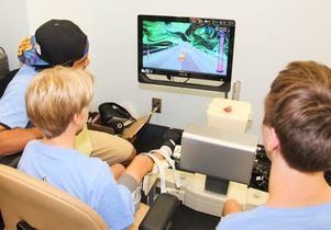 Niko plays a video game using his ankle to move the cursor as camp counselor Oliver (left) and student volunteer Ky Soriano watch.