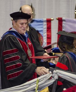 UNM president Robert Frank hands out a diploma and congratulates a graduate at commencement.