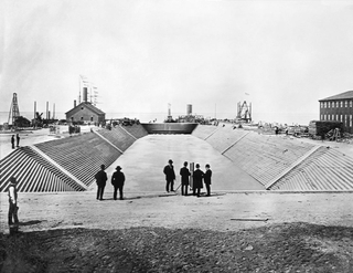 Dry Dock 1 at Newport News Shipbuilding is flooded prior to the official opening celebration of the shipyard's first dry dock on April 24, 1889. The Puritan-class monitor USS Puritan waits beyond the dry dock’s gate to enter. Dry Dock 1 at Newport News Shipbuilding